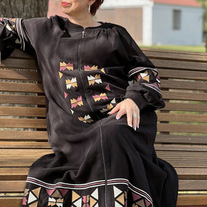 Salma-embroidered-zip-front-long-coat-abaya-with-side-pockets-in-black-sitting-on-bench