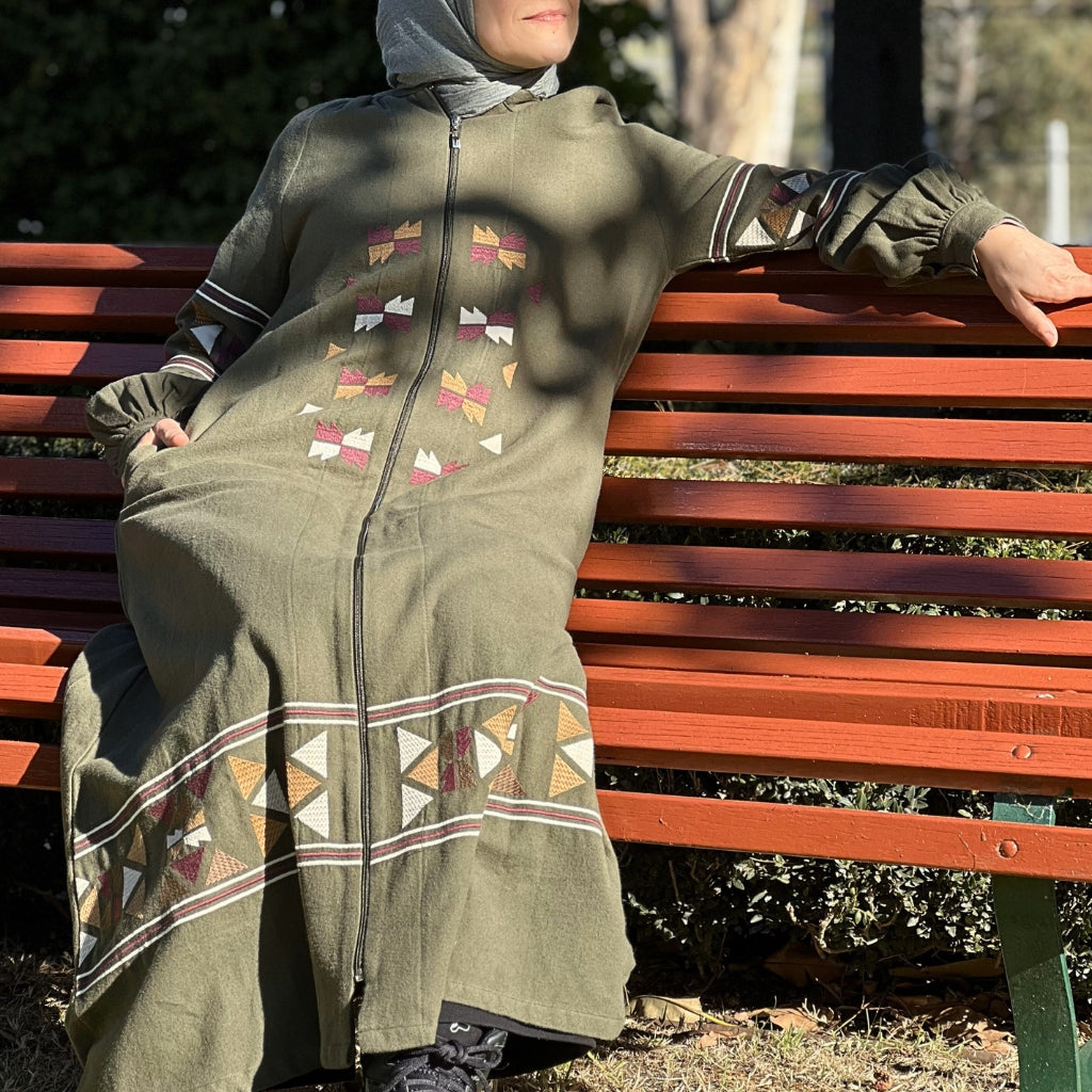 Salma-embroidered-zip-front-long-coat-abaya-with-side-pockets-in-khaki-sitting-on-bench