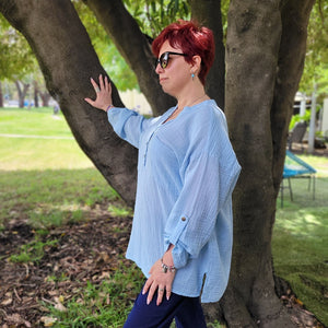 Ada-long-sleeve-Vneck-muslin-blouse-features-front-pockets-and-sleeve-tabs-in-ice-blue-worn-with-navy-casual-pants-side-view