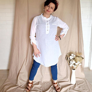 button-front-band-collar-tunic-shirt-with-button-tab-long-sleeves-mid-length-curved-hem-in-white-worn-with-jean-leggings-front-view