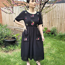 Load image into Gallery viewer, ashley-embroidered-midi-dress-with-embroidery-and-lace-detail-on-bodice-and-front-pockets-and-lace-on-hem-trim-in-black-front-of-tree-2
