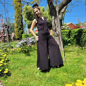 cotton-palazzo-pants-with-extra-wide-leg-fitted-mid-waist-elasticated-at-back-and-side-pockets-in-black-front-of-tree-side-view-2