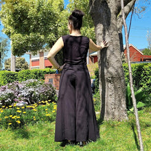 Load image into Gallery viewer, cotton-palazzo-pants-with-extra-wide-leg-fitted-mid-waist-elasticated-at-back-and-side-pockets-in-black-front-of-tree-back-view
