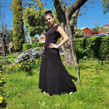 Load image into Gallery viewer, cotton-palazzo-pants-with-extra-wide-leg-fitted-mid-waist-elasticated-at-back-and-side-pockets-in-black-front-of-tree-side-view
