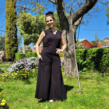 Load image into Gallery viewer, cotton-palazzo-pants-with-extra-wide-leg-fitted-mid-waist-elasticated-at-back-and-side-pockets-in-black-front-of-tree
