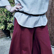 Load image into Gallery viewer, cotton-palazzo-pants-with-extra-wide-leg-fitted-mid-waist-elasticated-at-back-and-side-pockets-in-burgundy-worn-with-amber-tunic-blouse-light-grey-front-of-gate-close-up-2
