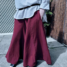 Load image into Gallery viewer, cotton-palazzo-pants-with-extra-wide-leg-fitted-mid-waist-elasticated-at-back-and-side-pockets-in-burgundy-worn-with-amber-tunic-blouse-light-grey-front-of-gate-close-up
