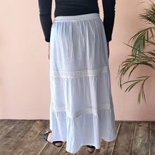 Load image into Gallery viewer, dahlia-tiered-maxi-skirt-with-lace-trim-in-white-worn-with-black-top-and-sandals-back-view
