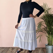 Load image into Gallery viewer, dahlia-tiered-maxi-skirt-with-lace-trim-in-white-worn-with-black-top-and-flat-sandals-front-view
