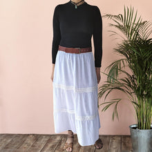 Load image into Gallery viewer, dahlia-tiered-maxi-skirt-with-lace-trim-in-white-worn-with-black-top-and-wide-brown-leather-belt-and-flat-sandals-front-view
