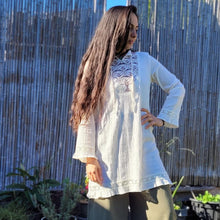 Load image into Gallery viewer, selena-long-sleeve-tunic-with-round-string-tie-neck-embroidery-on-chest-panel-and-lace-detail-and-ruffles-on-the-sleeve-ends-and-hemline-in-cream-outdoor-front-view
