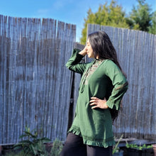 Load image into Gallery viewer, selena-long-sleeve-tunic-with-round-string-tie-neck-embroidery-on-chest-panel-and-lace-detail-and-ruffles-on-the-sleeve-ends-and-hemline-in-green-outdoor-natural-light-view
