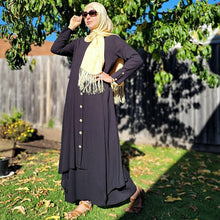 Load image into Gallery viewer, zahra-asymmetric-maxi-dress-with-layered-asymmetric-skirt-button-detail-on-front-in-black-in-front-of-tree
